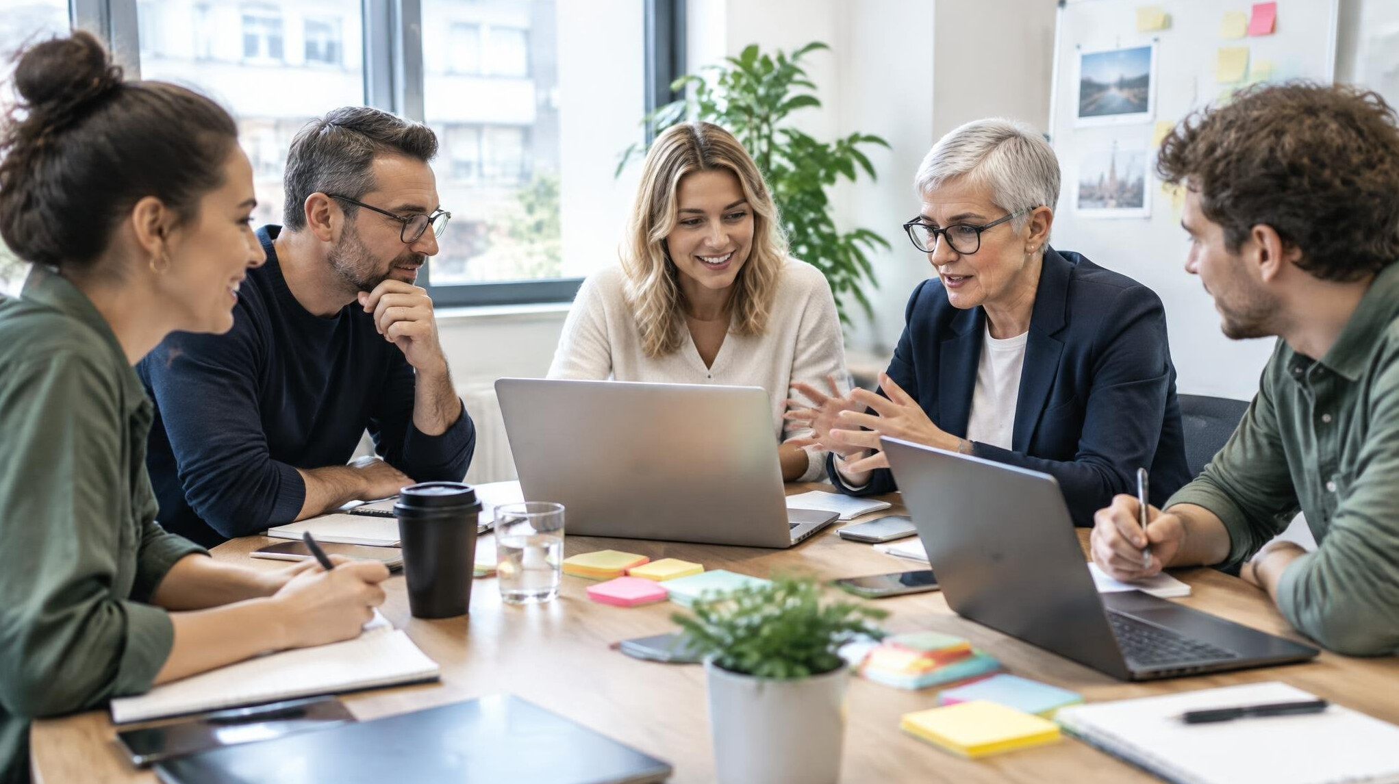Diverse group of professionals collaborating around a table with laptops and notes